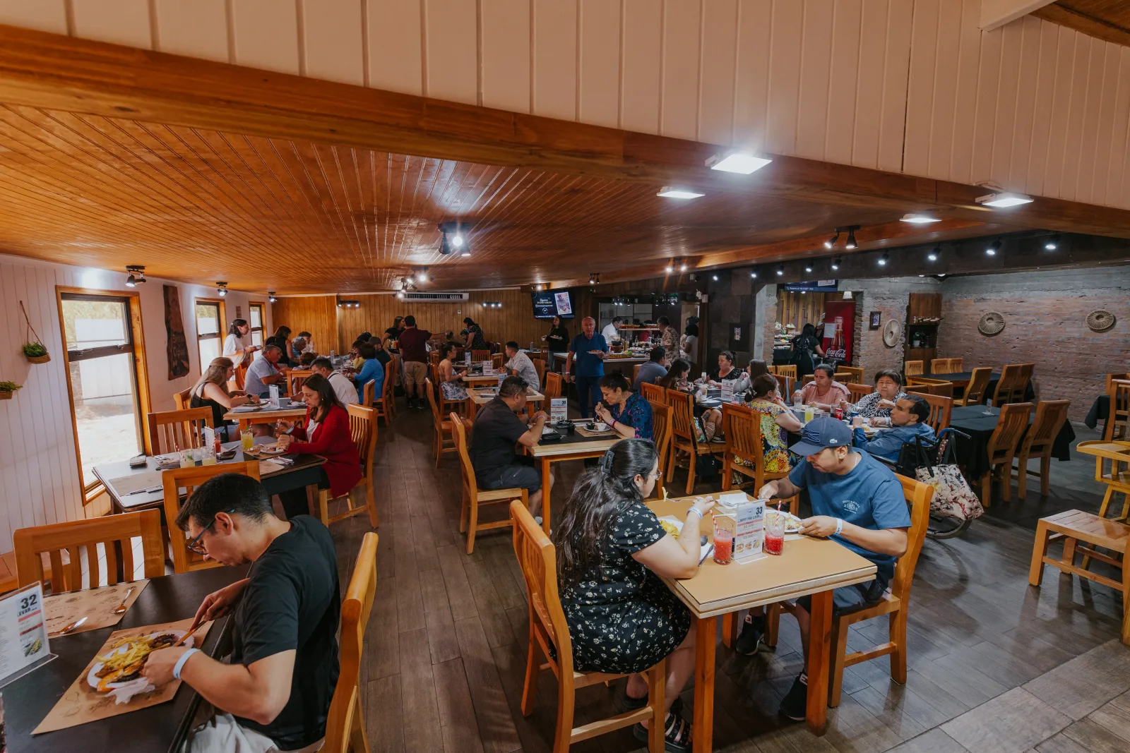 Salón cálido de madera con familias compartiendo almuerzo en mesas