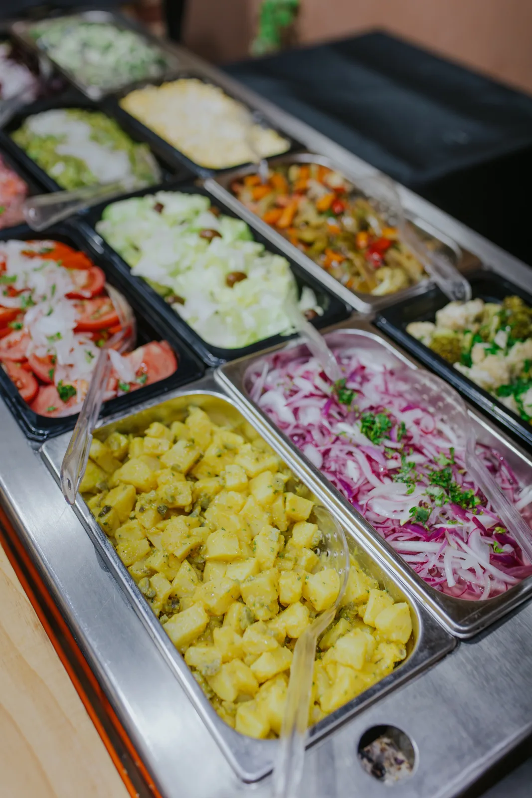 Barra de ensaladas frescas con tomate, papas, cebolla morada y verduras variadas