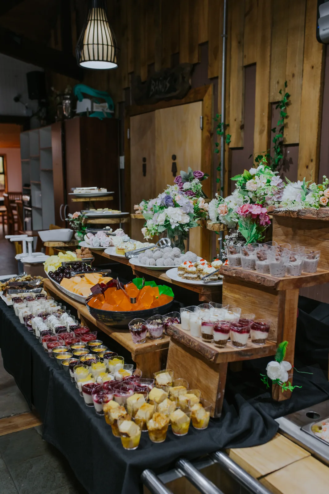 Mesa buffet de postres con variedad de mini tortas, mousses y vasitos decorada con arreglos florales